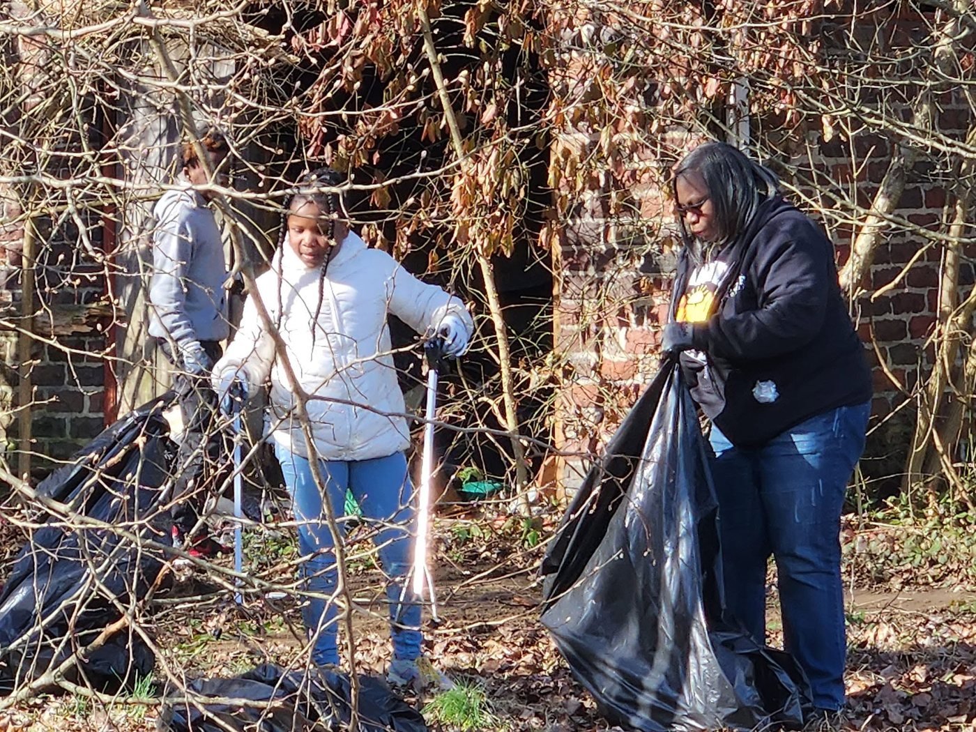 Two Do Not Be A Litterbug volunteers in gloves bagging litter from a brushy Dayton lot